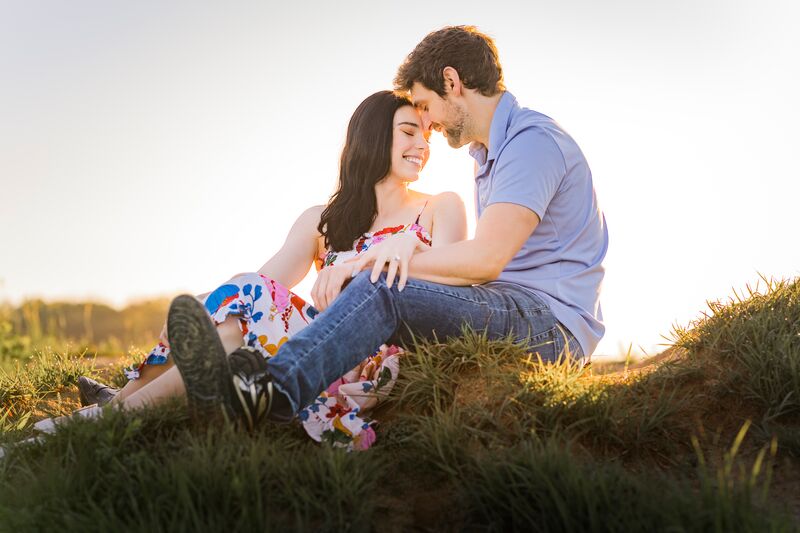 Theresa and Ryan sitting together in tall grass at sunset, laughing