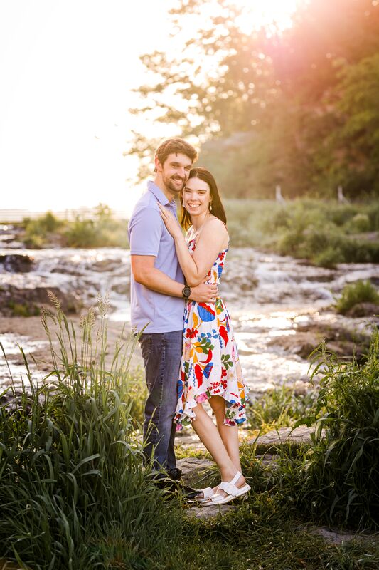 Theresa and Ryan embracing beside a rocky stream, tall grass in the foreground
