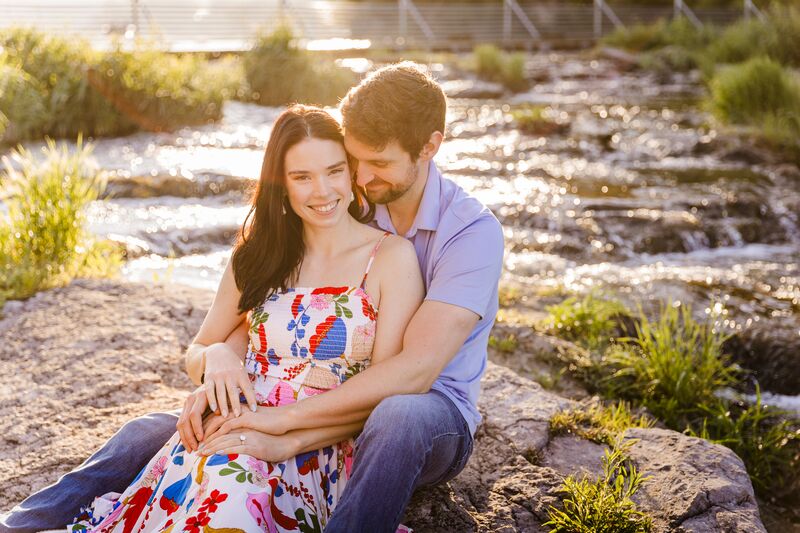 Theresa and Ryan sitting together by a rocky stream, her leaning back against him