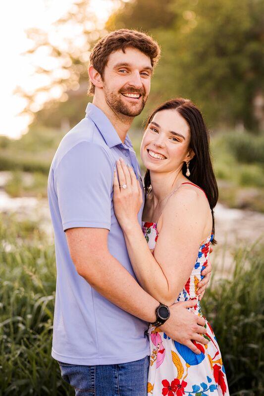 Theresa and Ryan smiling and embracing outdoors near a stream